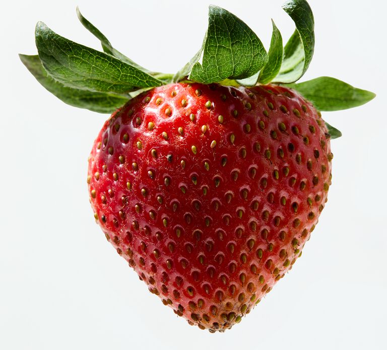 Close-up of a ripe red strawberry with green leaves against a light background