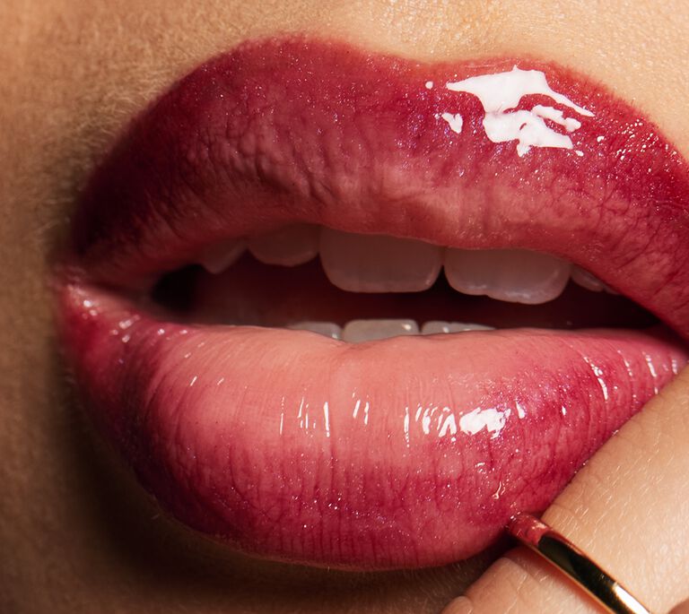 Pair of glossy, berry‑tinted lips with a finger touching the lower lip